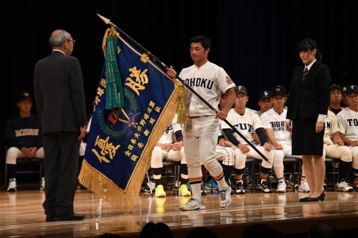 壇上に並ぶ各校の主将が見つめる中、優勝旗返還を行う岩﨑主将（中央）