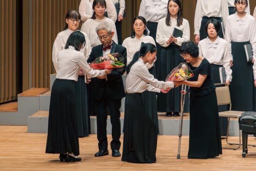花束を受け取る客演指揮の石川浩先生(左)と客演ピアニストの伊藤真奈美先生(右)。花束をお渡ししたのは、初等教育3年三浦実紗(左)と福祉心理学科2年大河原千聖(右)