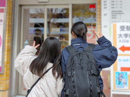 試験会場入り口で見送る教員にピースサインをして教室へ向かう学生たち