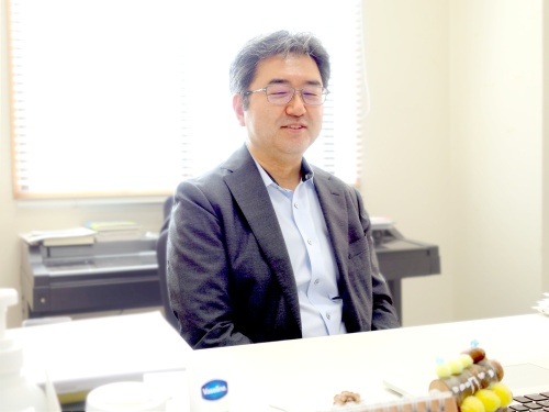 研究室の仕事机で微笑む佐藤先生