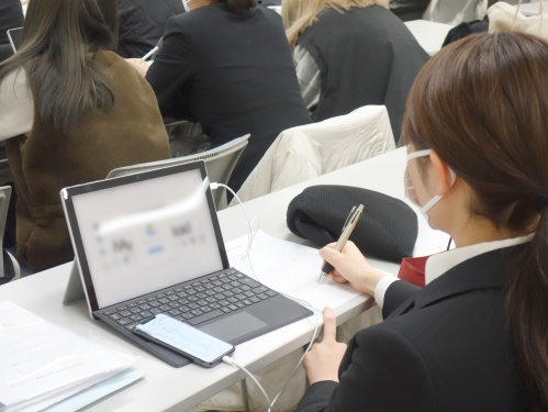 ノートを取り、スマホで報告会の次第を確認し、PCで分からない用語などを調べる学生の様子