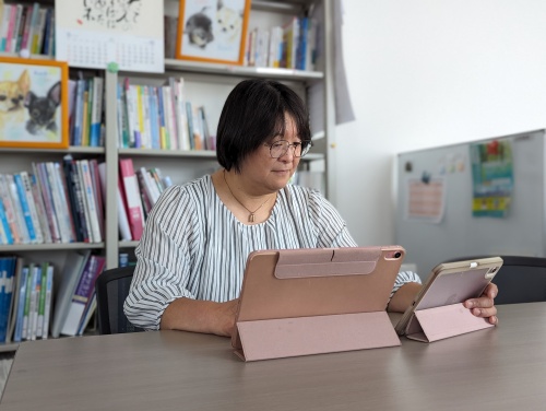 研究室の書架の前で2台のiPadで仕事をする太田先生