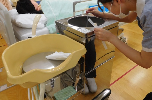 ベッド上でも行える洗髪車で洗髪を行いました。お湯の温度を測り確認しています。
