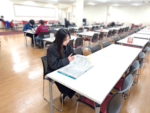 学食の奥のラーニングコモンズで資料をめくる庄司さん