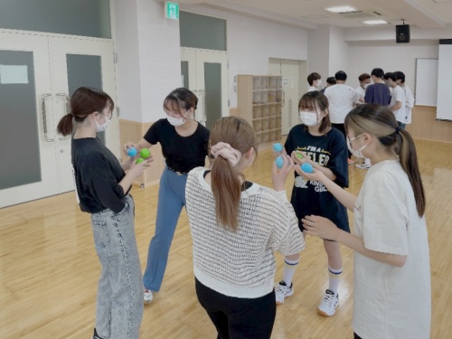 ライフキネティック講習会の様子。青いボールは「自分の名前」、緑のボールは「自分の好きな食べ物」を言ってから、次の人にボールを渡します。ボールが増え、手元がボールでいっぱいになってしまう人も続出。失敗しても学生みんなが楽しそう。笑顔がたくさんみられました。