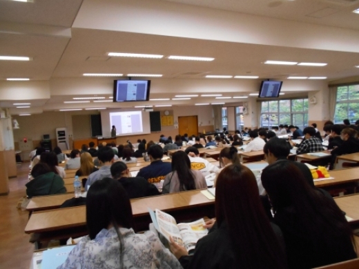 5/8　手元に配られた資料とモニターを見ながら施設の説明を聞く学生たち