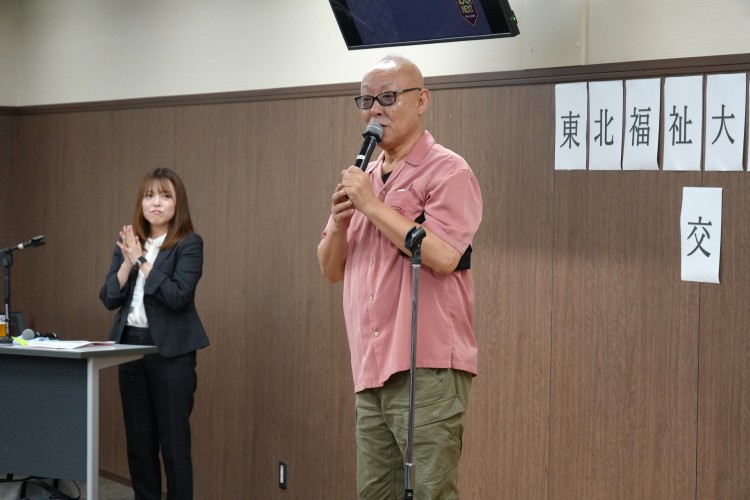 交流会で司会の名護ひと美さんと挨拶する本間明彦さん