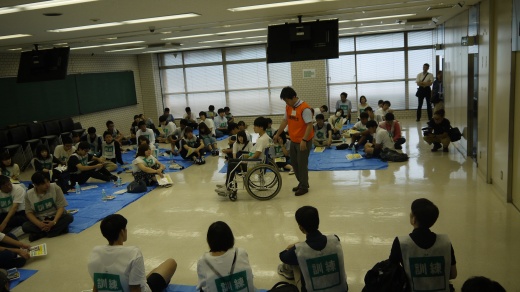 仙台駅東口キャンパスで、大勢の学生を前に車いす誘導について説明するスタッフ