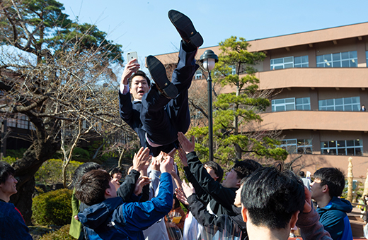 卒業式を終え、後輩から胴上げされる学生